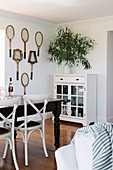 Dark dining table with white chairs and display cabinet, old tennis rackets as wall decoration