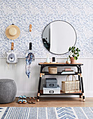 Storage idea in the hallway: table, round mirror above and wall hooks on blue and white wallpaper