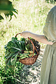 Frau hält Weidenkorb mit frisch geerntetem Gartengemüse
