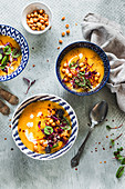 Creamy carrot parsnip soup with sorrel, chickpeas and microgreens served in blue bowls on gray background
