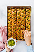 Woman sprinkling pistachio over newly baked baklava