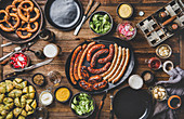 Octoberfest dinner table concept with grilled meat sausages, German pretzel pastry, potatoes, cucumber salad, sauces, beers in bottles and glasses