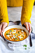 Autumn pumpkin soup with cream and feta cheese kept by a person in a yellow sweater