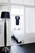 Black floor lamp in front of a glass room divider, with a view into the bedroom