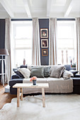 Sofa mit Kissen und Holzbank als Couchtisch im Wohnzimmer mit grauer Wand
