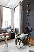 Classic chair below collection of hunting trophies on dark wall in living room