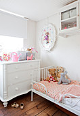 Weiße Kommode und zierliches Bett mit Kuscheltieren im Kinderzimmer