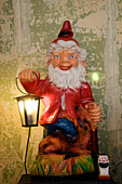 Kitsch lamp made from garden gnome holding lantern against battered wall