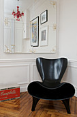 Modern black designer armchair in front of a wall with wainscotting and mirrors