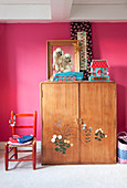 Old wooden wardrobe with floral motifs on doors against hot-pink wall in girl's bedroom