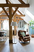 Vintage leather armchair next to a floor lamp in an open living room with rustic wooden beams