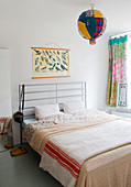 Double bed with metal headboard, poster of bird and spherical lamp with colourful fabric lampshade