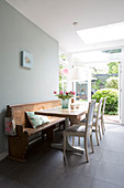 Wooden table with white chairs and old wooden bench on grey tiled floor