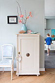 Chair next to old cupboard with accessories in pastel shades and boy in background