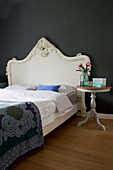 Bed with Baroque headboard and pedestal table against black wall