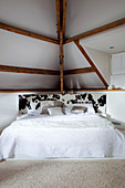 Bed with piebald cowhide headboard below sloping ceiling with exposed wooden beams