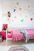 Colourful love-harts on wall above bed with lacy pink blanket in girl's bedrm