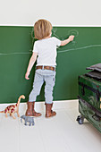 Little boy drawing on green chalkboard in bedroom