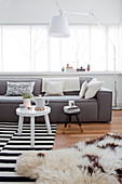 Pale grey sofa and standard lamp in front of window and side table on black-and-white striped rug