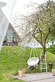 White chair hanging from a tree in the garden