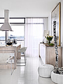 Kitchen island with white bar stools, leather poufs, and sideboard in an open plan kitchen