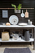 Console table with kitchen utensils and pouring cans in front of a dark wooden wall on the terrace