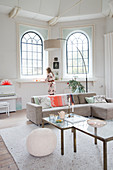 Sofa, set of coffee tables and arc lamp in front of arched windows in living room with woman in background