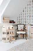 Dolls' house and Baroque chair in room with sloping ceiling and wallpaper with pattern of bird nesting boxes