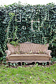 Altes Sofa vor der Gartenmauer mit Efeu und Bilderrahmen