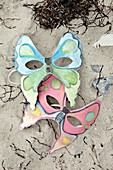 Selbstgemachte Masken mit Schmetterling-Motiv im Sand