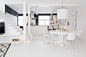 Round table with various chairs in front of the kitchen island and stairs in a white, open living room