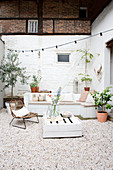 Wooden bench, pallet table, and chair on the terrace with a white brick wall and gravel floor
