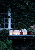 Laternen aus weißem Papier auf altem Tisch vorm Gartenhaus mit Efeu