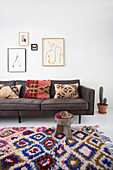 Colourful carpet in front of grey sofa with ethno cushions and picture gallery