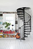 A black spiral staircase next to a guitar and a bookshelf