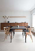 A black dining table with chairs in front of a brown sideboard