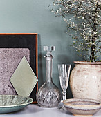 Kristallkaraffe und Glas, Keramikgefäß mit Bäumchen und Schalen auf Ablage