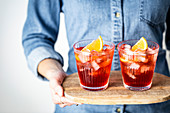 Negroni cocktail on a wooden tray, held by a person in a denim shirt