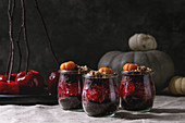 Layered Halloween dessert chocolate biscuit, raspberry jelly, nuts, marzipan pumpkin in glass jars and red caramel apples on branches