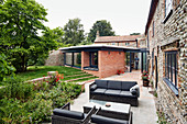 Blick über Terrasse mit Outdoor-Möbeln auf Anbau aus Ziegelsteinen und auf bestehendes Bauernhaus