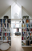 Bookshelves in a partition wall under the sloping roof with a view of a bedroom