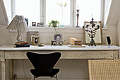 Designerstuhl am alten weißen Schreibtisch mit Fotos unterm Dachfenster