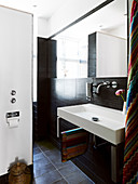 A square washbasin in a small bathroom with dark tiles