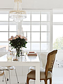 Baroque chair at the white table with bouquet of roses under the chandelier