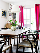 Designer chairs at a dining table in front of a window with pink curtains