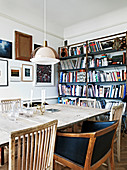 Different chairs at the dining table in front of the bookshelf and a salon style picture wall