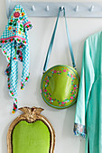A bag and a colourful scarf on a coat rack with a green chair below it