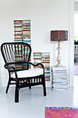 Black rattan chair in front of a pile of books and magazines with a table lamp