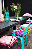 Bunte Stühle mit Sitzkissen um schwarzem Holztisch mit Laternen und Rosenstrauß