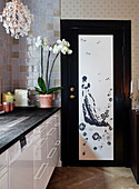 White kitchenette with black worktop, orchid, and chandelier, door with an Asian motif